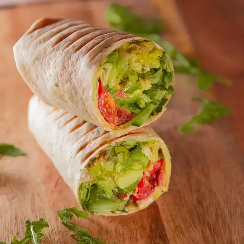 halbes Wrap mit mit Basilikumpesto, Salat, Avocado, Gurke, Tomate und Frühlingszwiebeln.